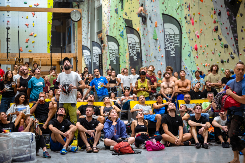 Clienti e appassionati guardano verso strapiombo per osservare gli atleti che arrampicano